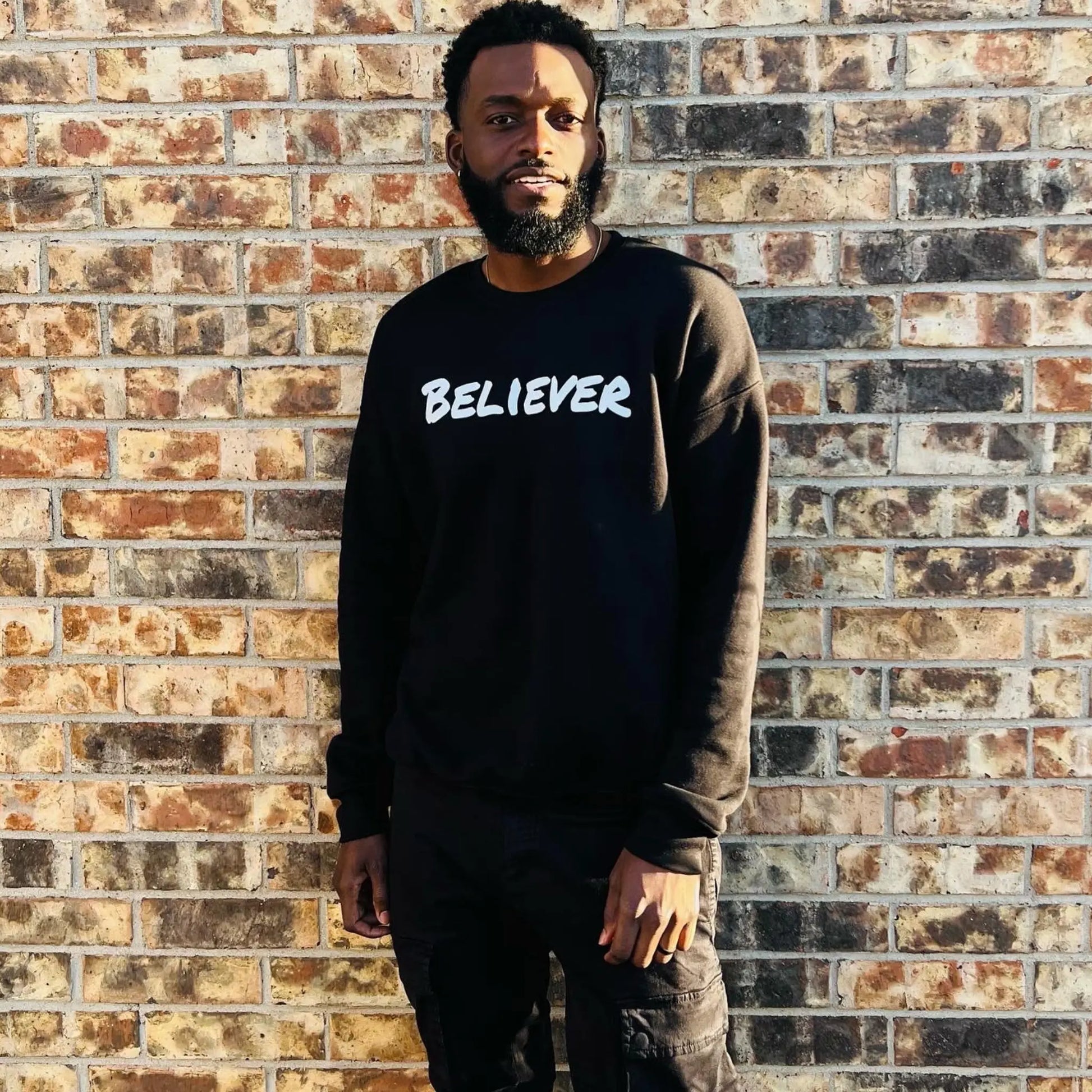 This Sweeatshirt is all black with a crew neck style. The words Believer are pressed on the shirt in bold white letters. Believer is written across the chest, stretching from sholder to shoulder. The sweatshirt this comftorable and fitted. Size up for a look. Edit alt text. On a Nuetral Colored back ground. The back reads John 3:16 on the tail of the sweatshirt.