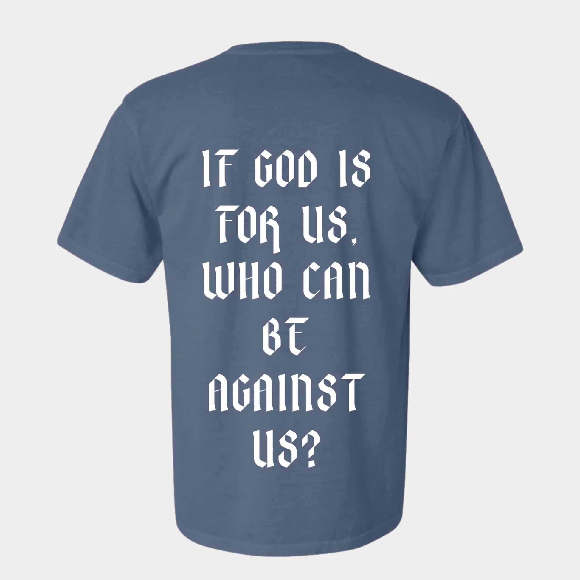 Romans 8:31 T-shirt is in the color blue jean, with a crew neck style. There is a crown logo on the left side of the chest. The Romans 8:31 T-shirt is comfortable and fitted. Size up for an oversized look. On a Neutral Colored background. The back reads “If God is for us who can be against us”, in bold white letters. Photos is taken outside in the sunslight.  Christian Clothing brand crown of favor