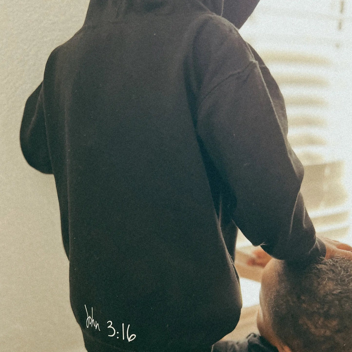 This hoodie is all black with a crew neck style. The words Believer are pressed on the shirt in bold white letters. Hoodie is written across the chest, stretching from sholder to shoulder. The Hoodie this comftorable and fitted. Size up for an oversized look. Edit alt text. On a Nuetral Colored back ground. The back reads John 3:16 on the tail of the Hoodie.