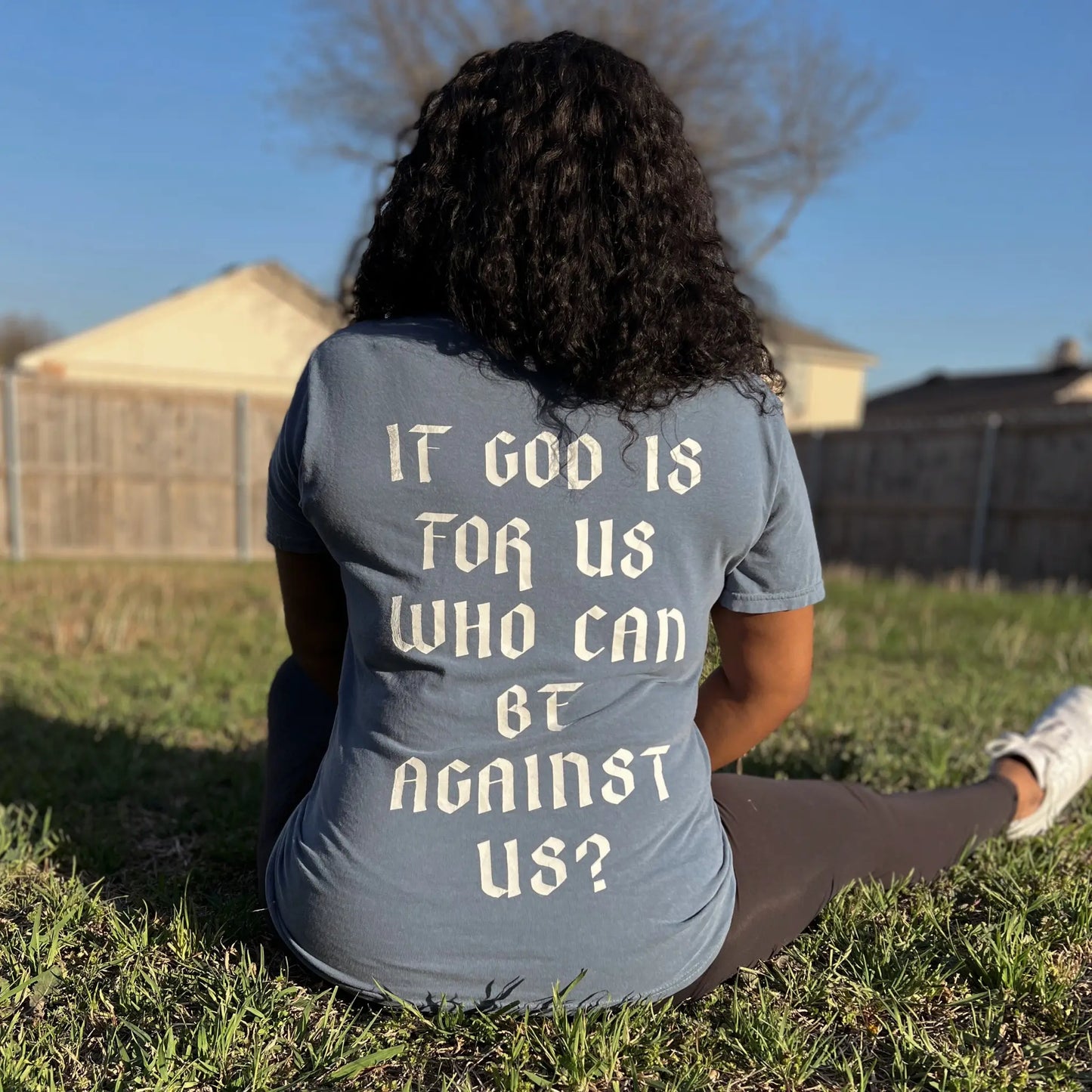 Romans 8:31 T-shirt is in the color blue jean, with a crew neck style. There is a crown logo on the left side of the chest. The Romans 8:31 T-shirt is comfortable and fitted. Size up for an oversized look. On a Neutral Colored background. The back reads “If God is for us who can be against us”, in bold white letters. Photos is taken outside in the sunslight. Christian Clothing brand crown of favor