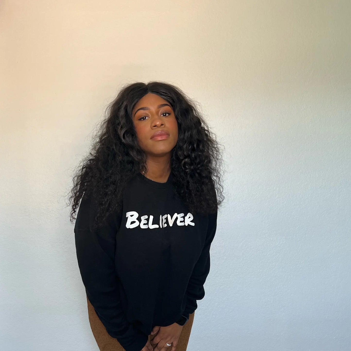This Sweeatshirt is all black with a crew neck style. The words Believer are pressed on the shirt in bold white letters. Believer is written across the chest, stretching from sholder to shoulder. The sweatshirt this comftorable and fitted. Size up for an oversized look. Edit alt text. On a Nuetral Colored back ground. The back reads John 3:16 on the tail of the sweatshirt. 